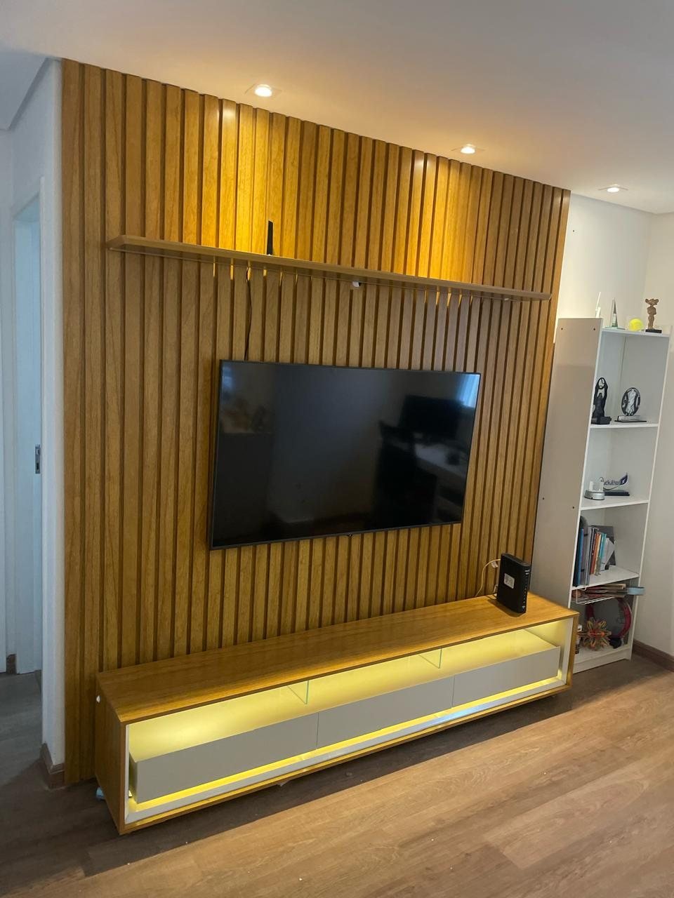 Painel ripado com televisão e rack iluminado em sala residencial