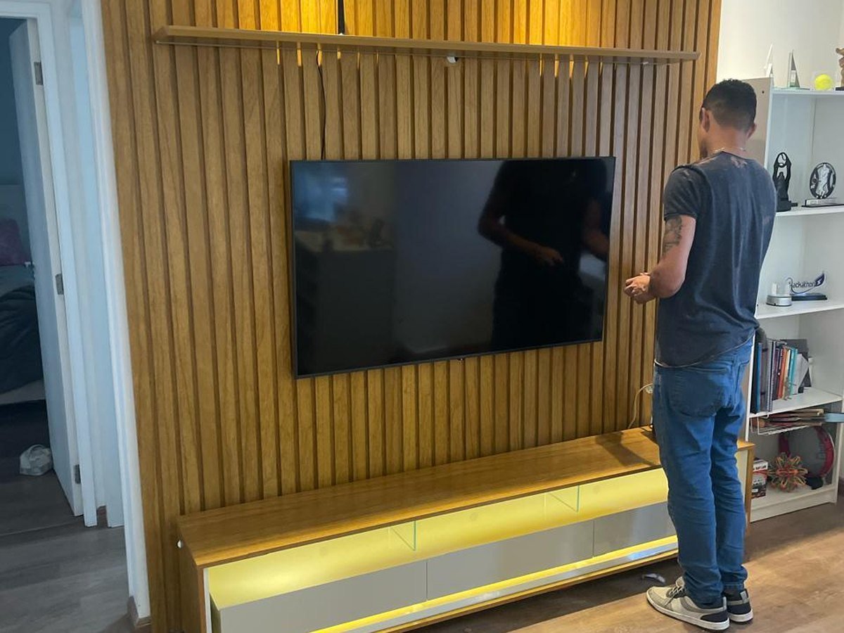 Profissional realizando ajuste técnico em painel ripado com televisão